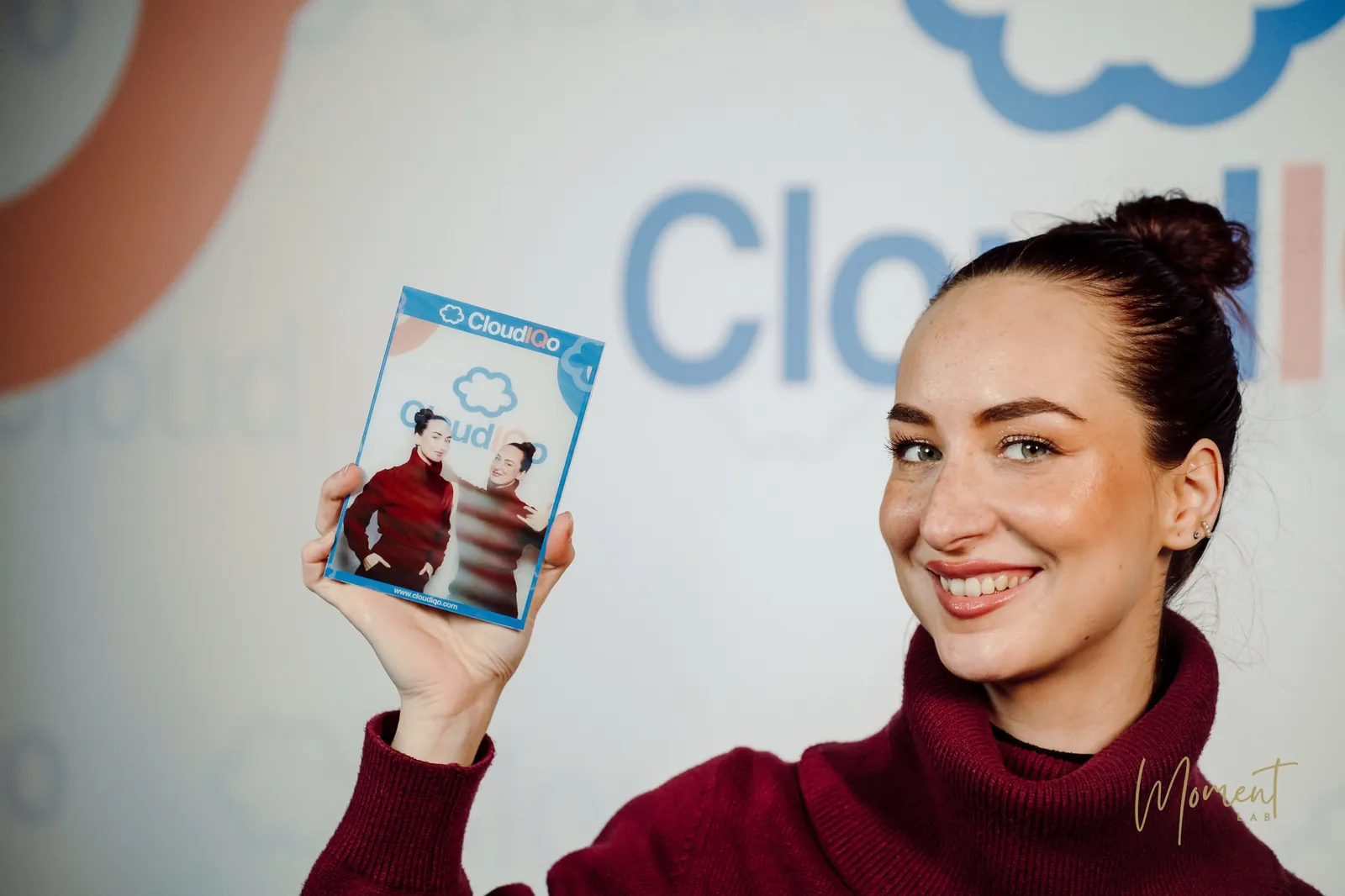 An attendee holding a branded photo booth print in front of the event backdrop