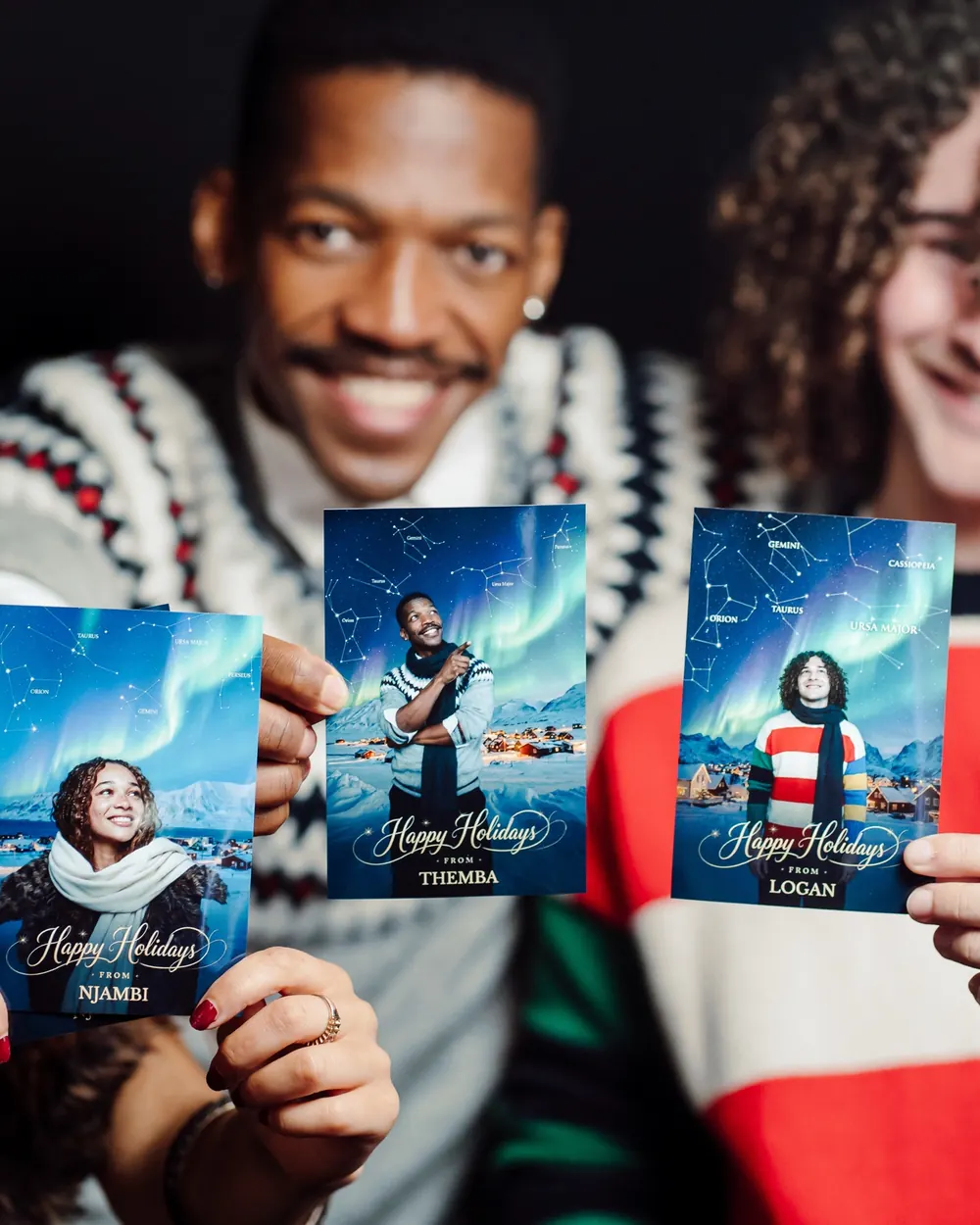 Three guests holding Holiday Constellation prints, each with their own starscape and northern lights