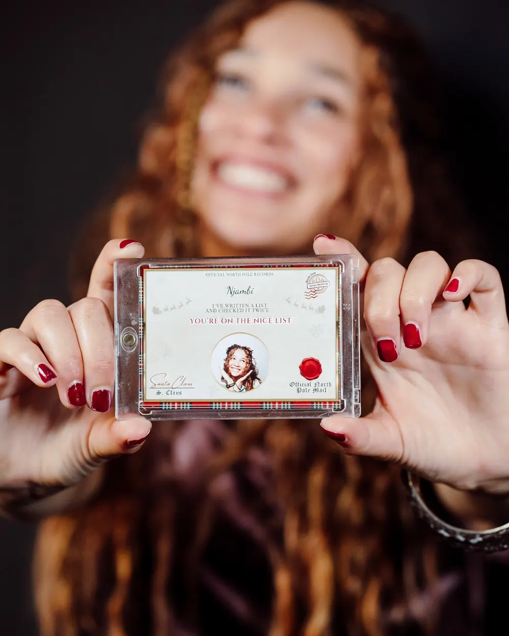 A personalised Nice List pass card with a guest's portrait, held in a clear keepsake case