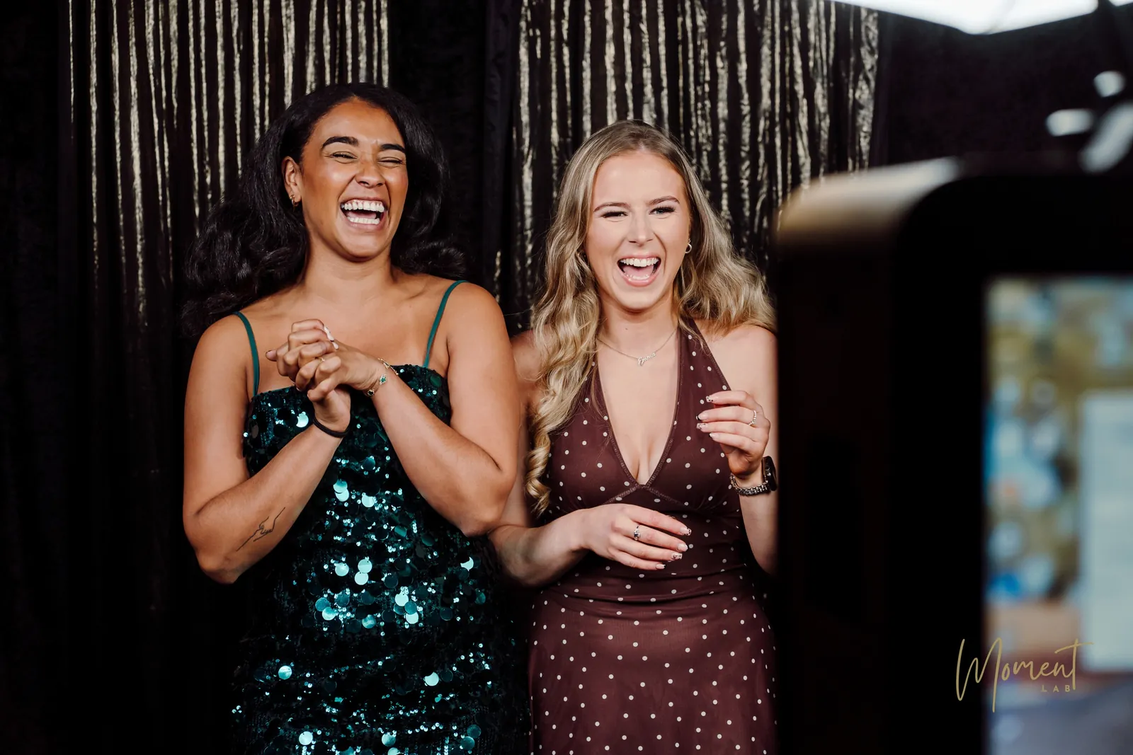 Two guests in evening dresses laughing as their photo appears on the booth screen