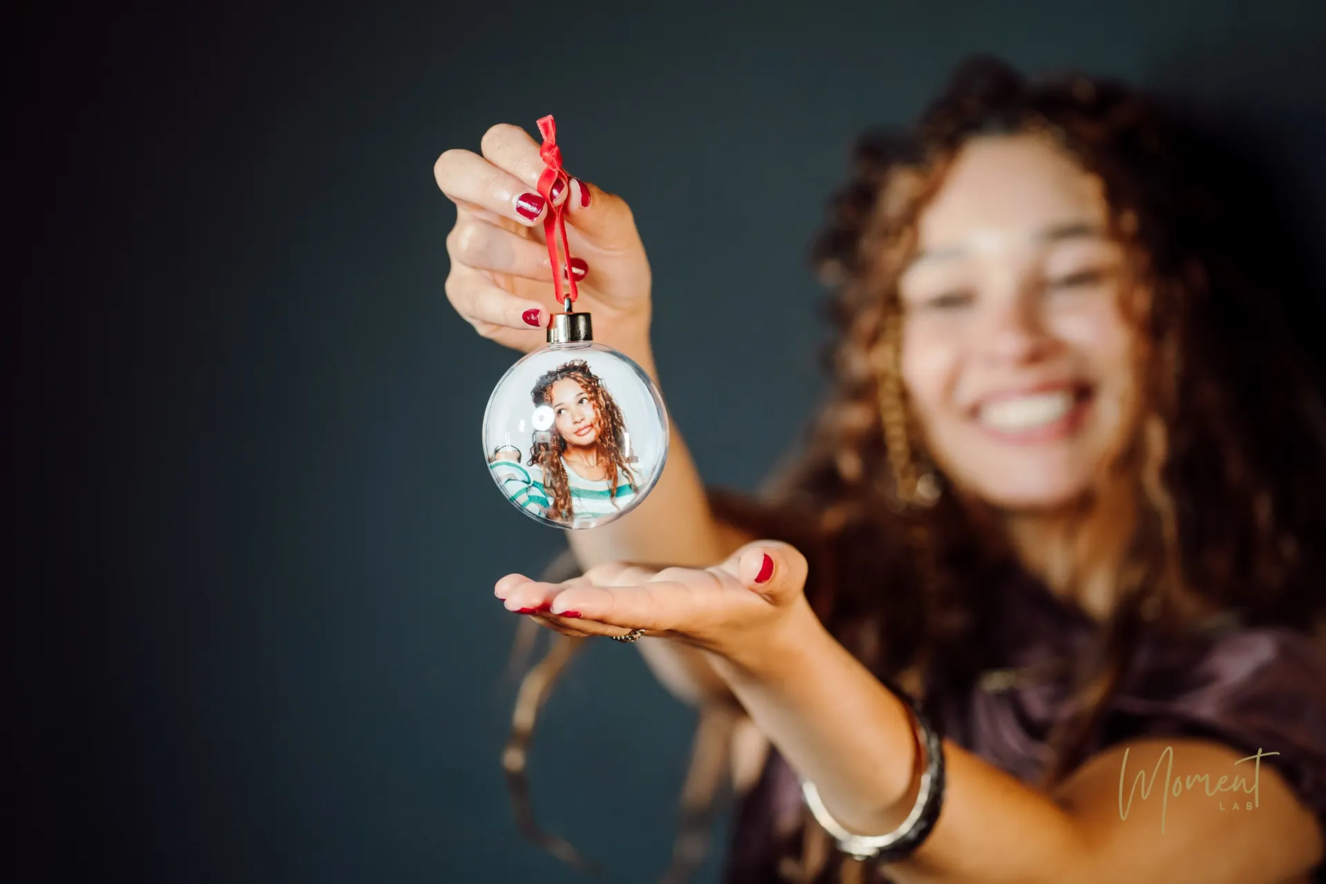 A guest holding a clear photo bauble with her portrait inside, tied with a red ribbon