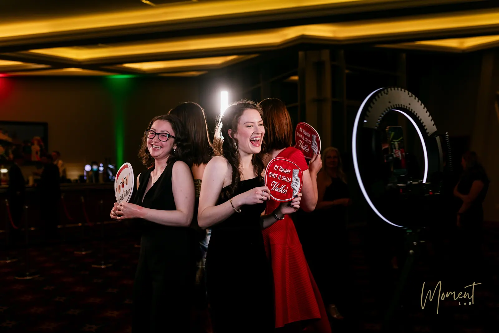 Guests laughing with festive props at The Spin 360 video booth, the ring light glowing beside them
