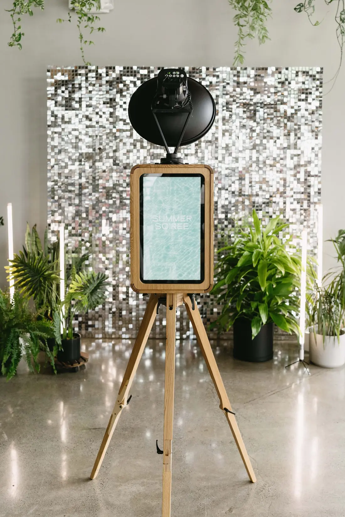 The Studio photo booth in natural oak with its studio light, set against a sequin wall and greenery