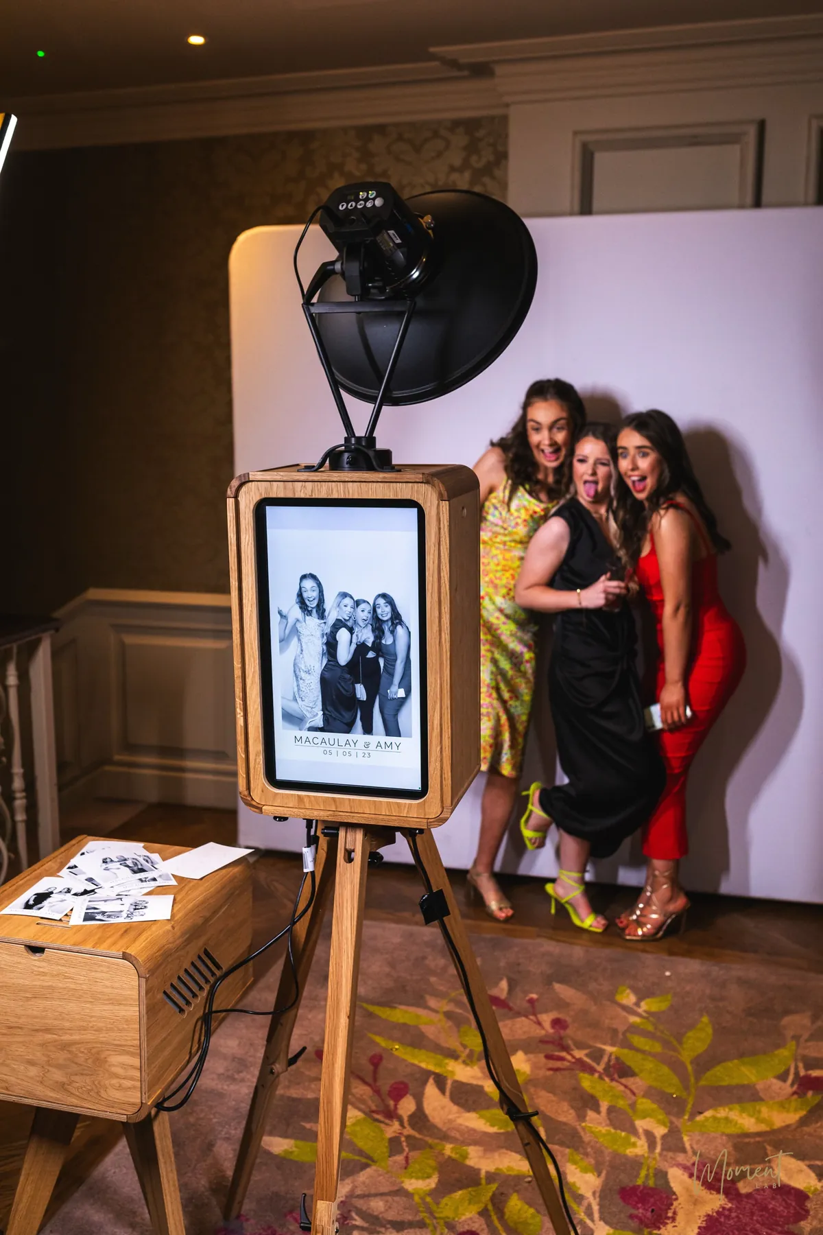 Wedding guests posing at The Studio open-air photo booth, their black and white print on the screen