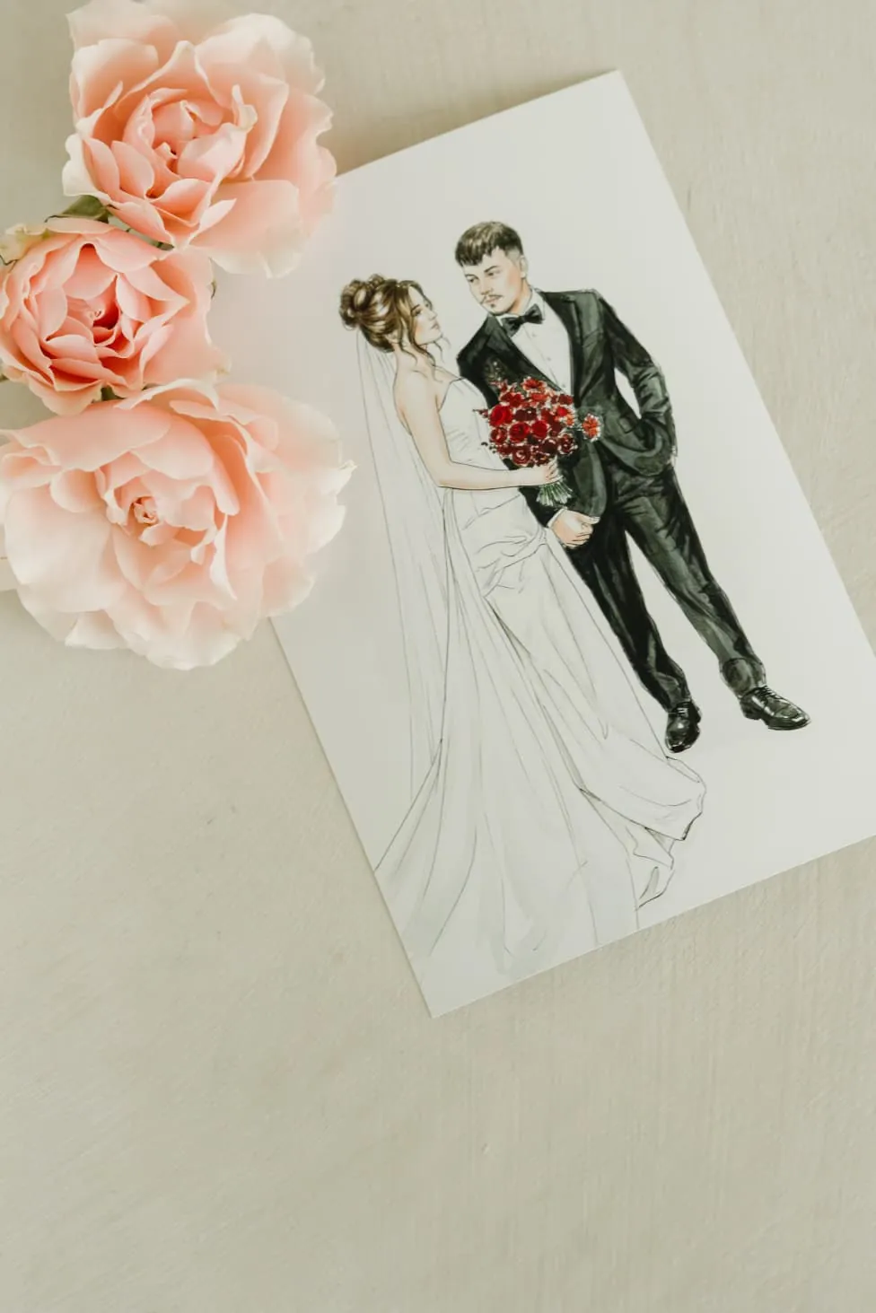 An illustrated wedding portrait print beside blush roses