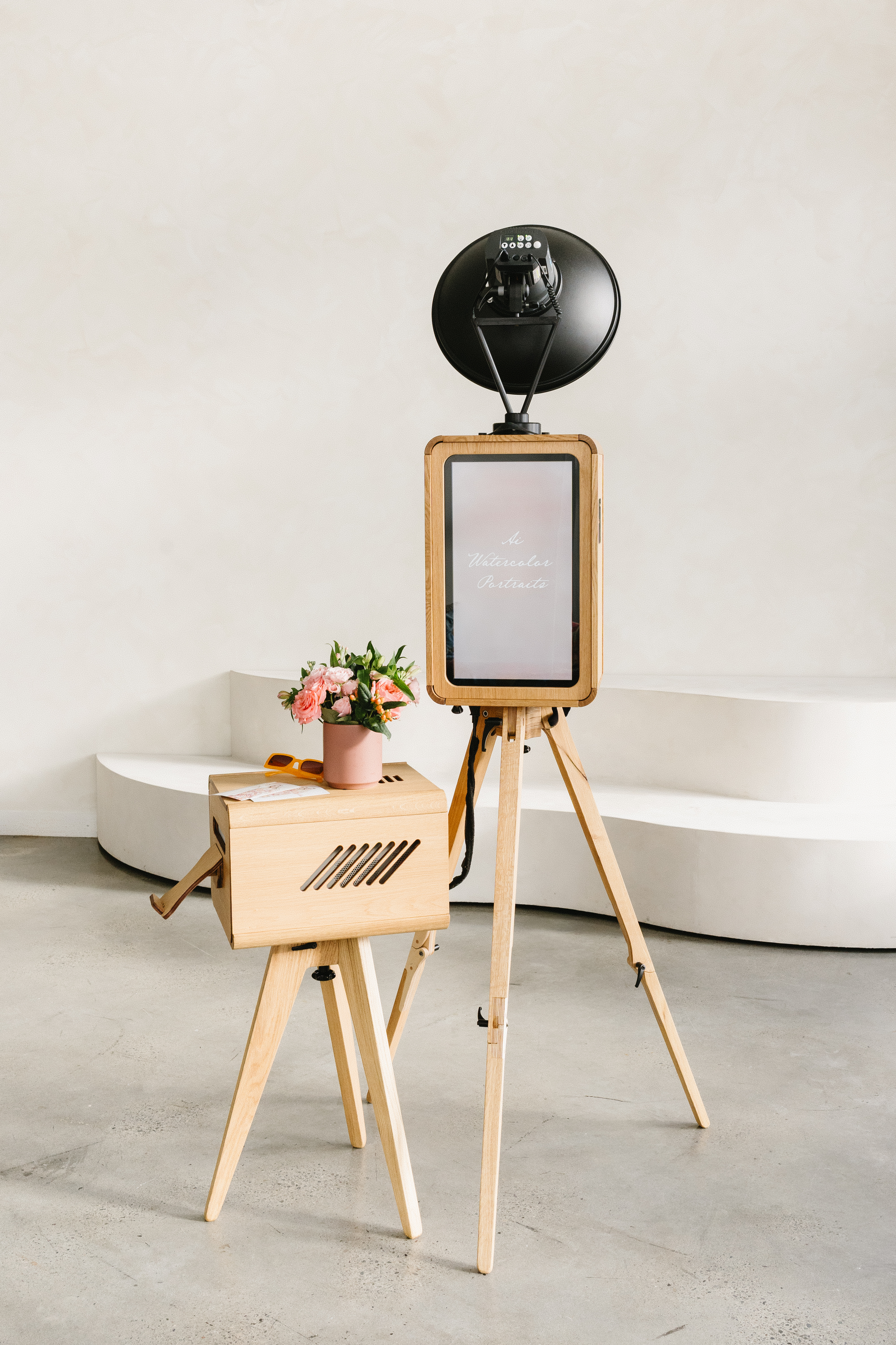 The Studio — a wooden open-air photobooth with a vertical touchscreen and professional lighting, styled with flowers and props